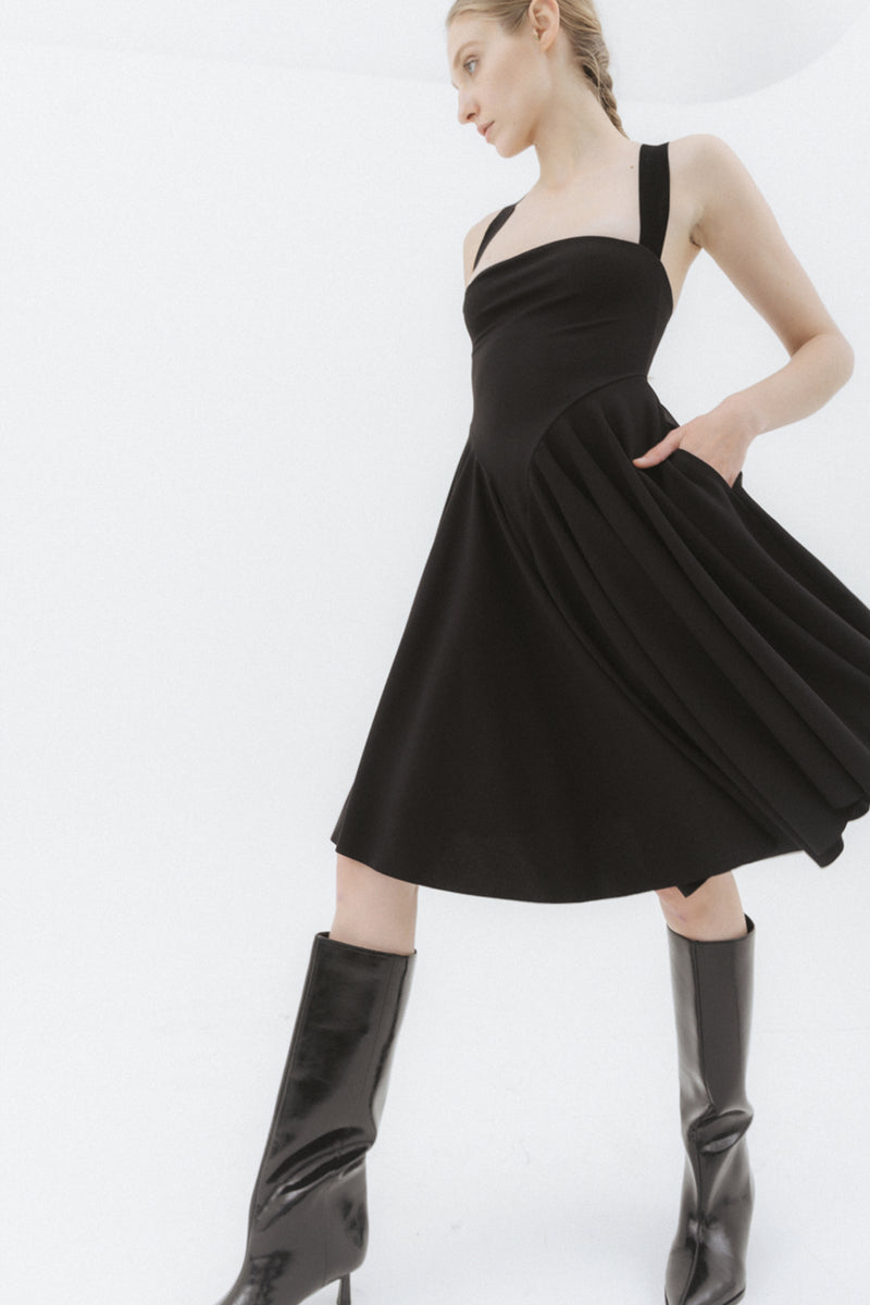 Blond woman wearing a black, pleated midi dress and knee-high black boots. 